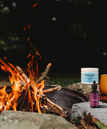 Campfire with a mug, cbd gummies and tincture bottle on a grassy area at night.